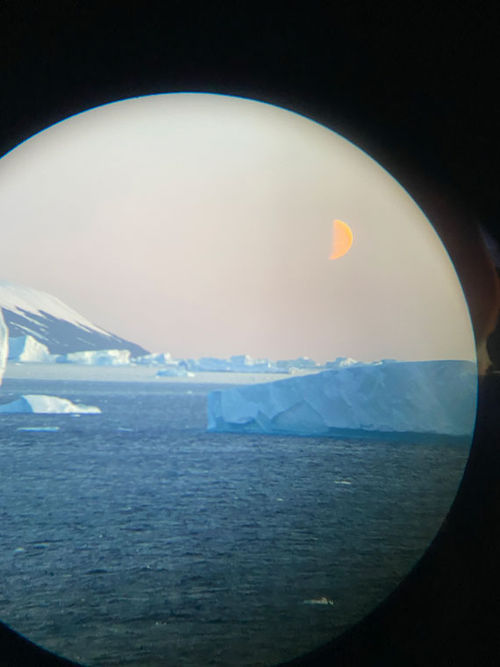 As seen through the lens of a pair of binoculars, a half-moon rises ahead of the bow of the Quark Ultramarine on its way to Antarctica.